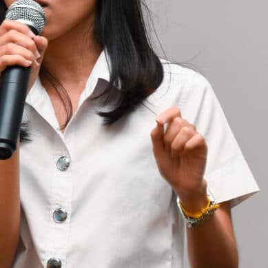 African American women in a white shirt talking into a microphone